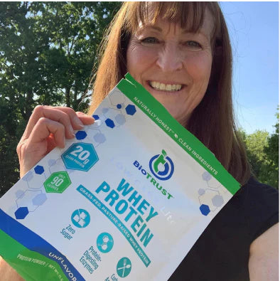 User generated content photo of smiling lady holding a bag of BioTRUST Whey Protein in front of trees with a blue sky background