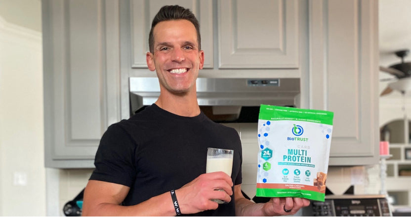 Photo of BioTRUST Head Coach Tim Skwiat holding a glass of salted caramel low carb multi-protein in his right hand and a bag of the product in his left hand